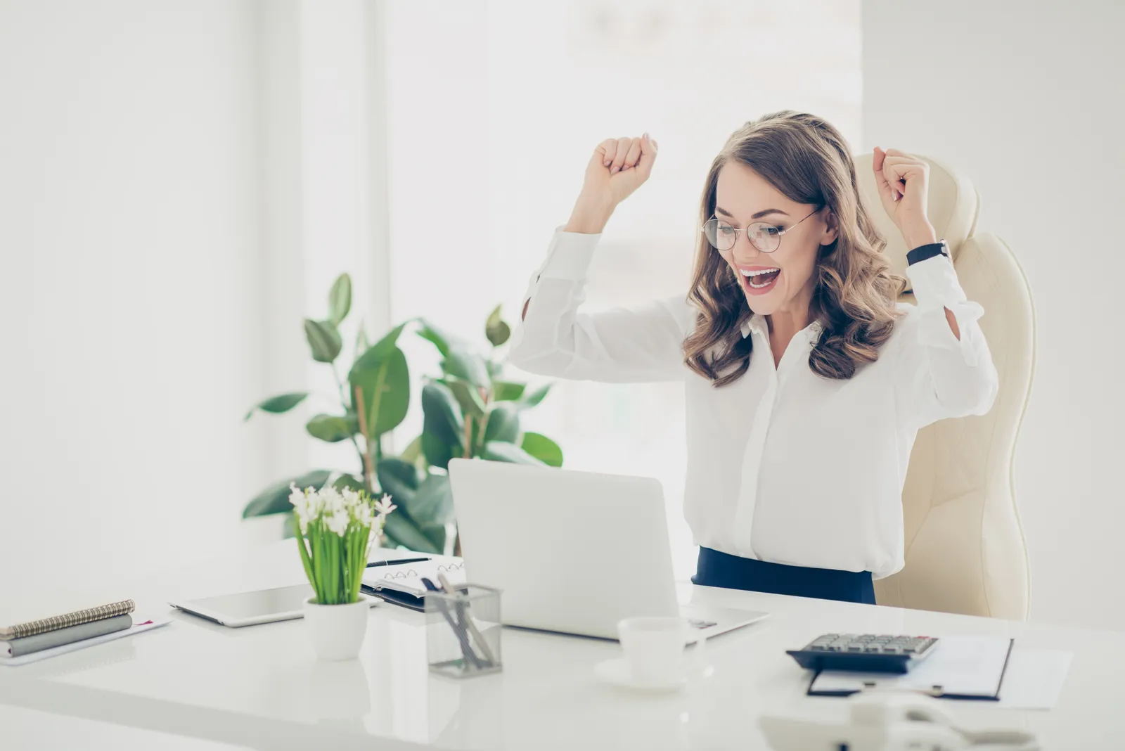 Portrait of lucky, charming, cheerful, positive, pretty, stylish, trendy brunette woman with curly hair looking at screen of laptop having her hands arms up celebrating completed project, presentation